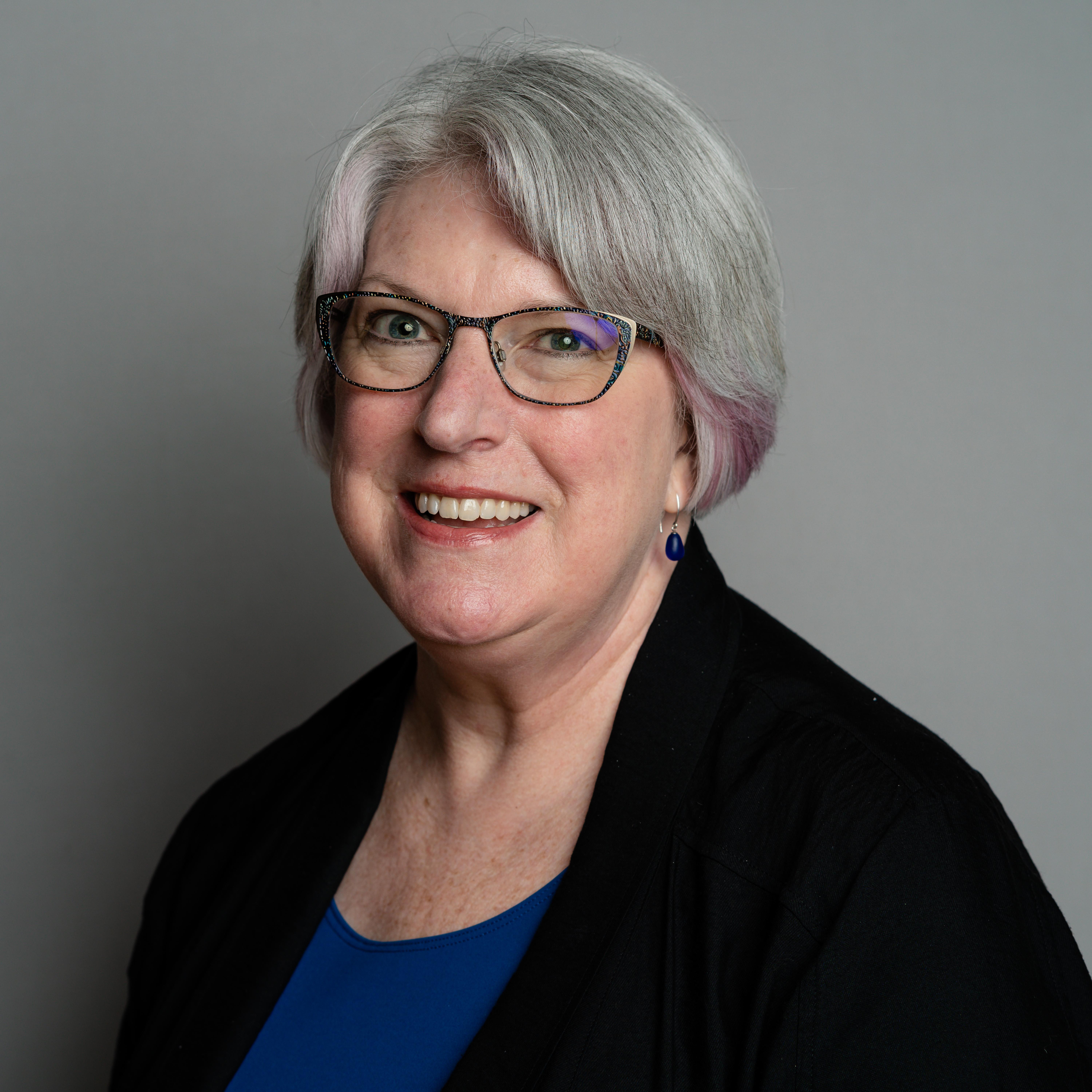 Professional portrait of a woman wearing a royal blue shirt, black shawl, and glasses.